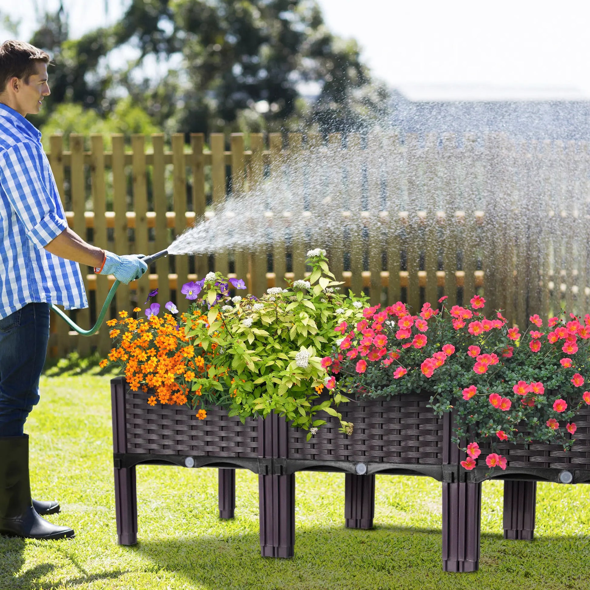 Person watering flowers in a raised garden bed with a hose.