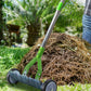 Dwellcozy rolling thatch rake for Lawns with green handle and wheels on a pile of straw in a garden setting.